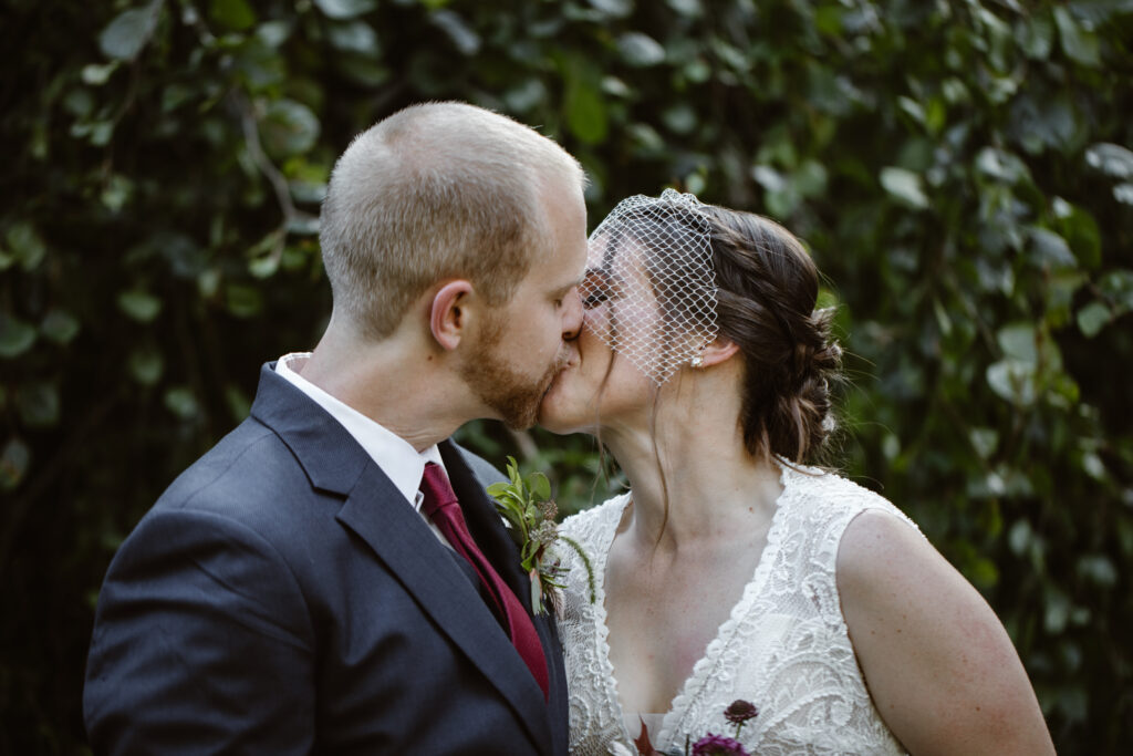 PA wedding couple among the evergreens sharing their first kiss